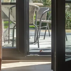 Geöffnete Terrassentür mit Blick auf moderne Gartenmöbel und sonnige Terrasse im Grünen.