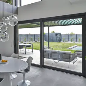 Modernes Esszimmer mit Blick durch große Glasfront auf Terrasse, Garten und Pool.
