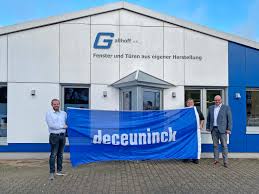 Drei Personen stehen vor einem Fenster- und Türen-Fachbetrieb und halten ein Deceuninck-Banner.