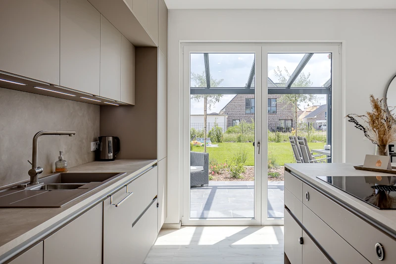 Moderne helle Küche mit Blick durch große Terrassentür auf gepflegten Garten und Terrasse.