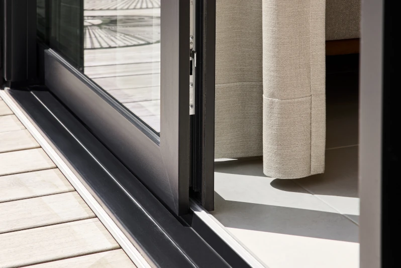 Moderne bodentiefe Schiebetür mit Aluminiumrahmen öffnet sich zur Terrasse mit Holzbelag.